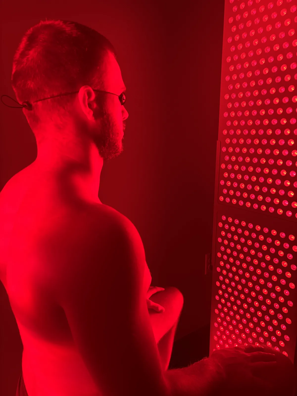 Patient with eye protection seated beside the red light therapy panel at Moveology 605